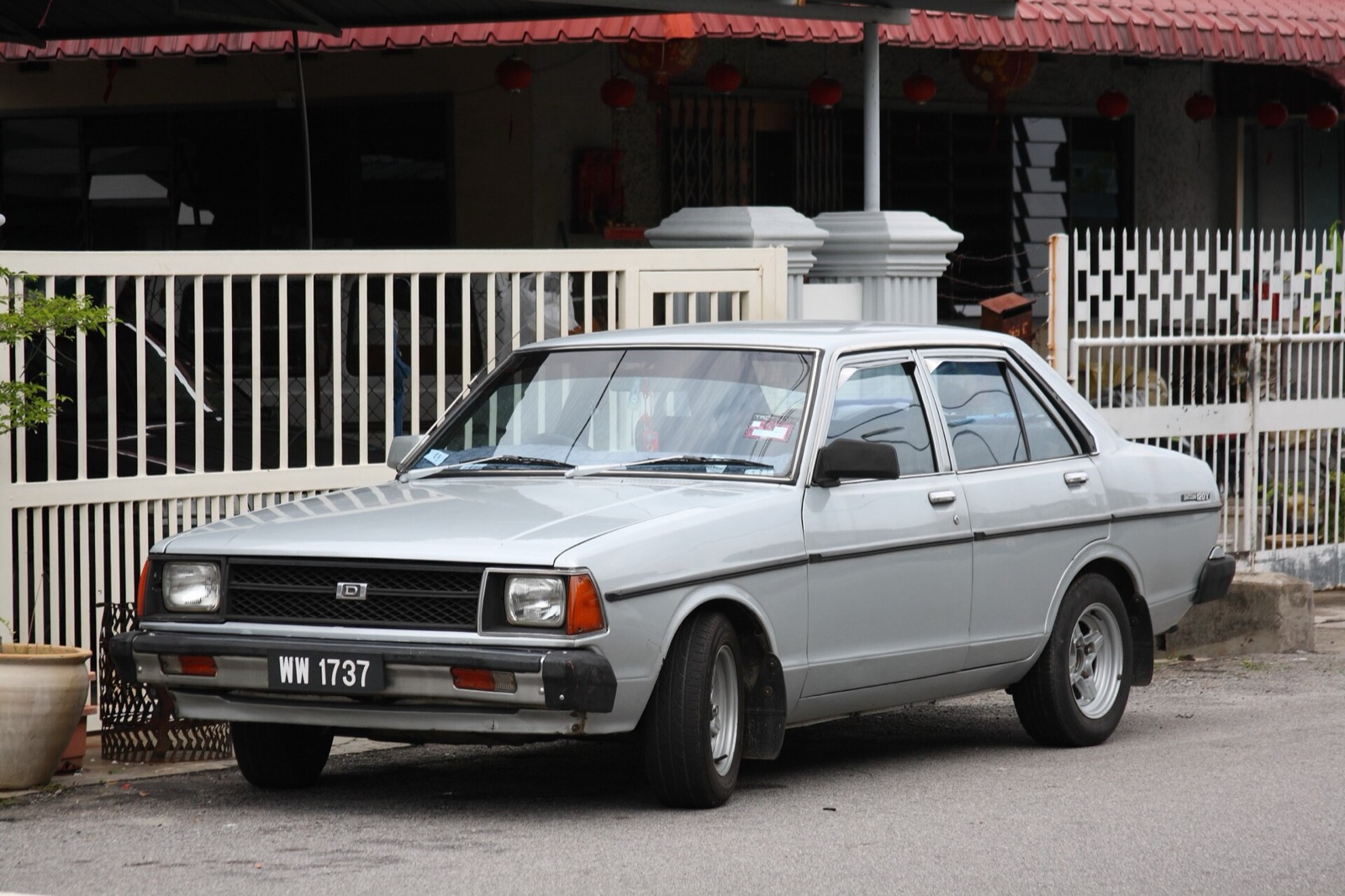 A silver Datsun sedan outside a terrace house in Malacca, Malaysia: Datsun was the marque Tan Chong & Co distributed in Malaysia from 1957